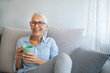 © Dragana Gordic - Happy lady relaxing at home with hot drink. Shot of a happy mature woman relaxing on the sofa with a warm beverage at home. Senior woman drinking hot drink sitting on sofa