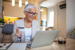 © Dragana Gordic - Mature Woman Holding Credit Card and Using Laptop Computer While Paying Bills at Home With Credit Card. E-banking Concept. Woman paying bills from home