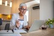 © Dragana Gordic - Happy senior woman making online payments of bill using laptop. Smiling mature woman shopping online with credit card. Pensioner holding credit card for internet banking and looking at camera.