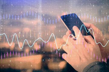 Double exposure of man's hands holding and using a digital device and forex graph drawing. Financial market concept.