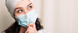 © Volodymyr - Interested focused nurse young medic standing and looking at the camera. Female doctor dressed in medical gown and surgical hat. Pandemic virus coronavirus concept, disposable face mask, copy space.
