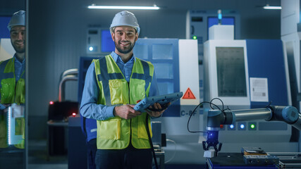 Fototapete - Portrait of Professional Engineer Wearing Safety Vest and Hardhat, Uses Industrial Digital Tablet to Program, Manipulates Robot Arm, Looks at Camera and Smiles. Factory Workshop with CNC Machinery