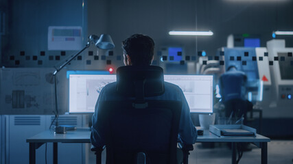 Industrial Engineer Solving Problems, Working on a Personal Computer, Two Monitor Screens Show CAD Software with 3D Prototype of Eco-Friendly Electric Engine Concept. Back View Shot