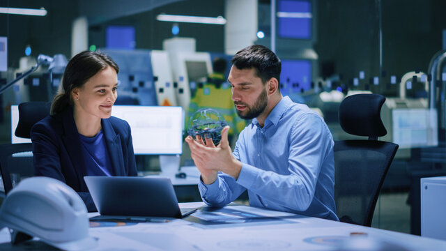 Industry 4.0 Modern Factory Meeting Room: Chief Engineer Holds Mechanism, Shows it to Female Designer, Use Laptop. Scientists in Contemporary Lab Build Electronic Machinery for With Futuristic Design