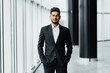 Handsome bearded Indian in a suit in the middle of the corridors of a modern office, modern building, manager, office worker