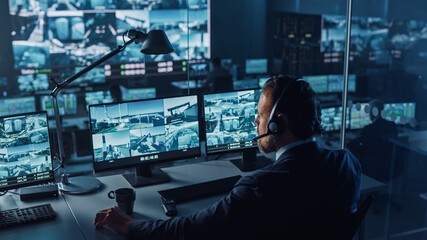 Fototapete - Male Officer Works on a Computer with Surveillance CCTV Video in a Harbour Monitoring Center with Multiple Cameras on a Big Digital Screen. Employees Sit in Front of Displays with Big Data.