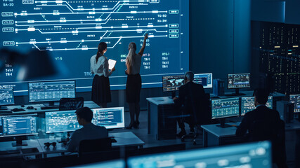 Poster - Two Software Engineers Talking Next to a Big Screen in a Modern Monitoring Office with Live Analysis Feed with Charts. Monitoring Room Big Data Scientists and Managers Sit in Front of Computers.