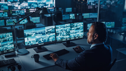 Wall Mural - Male Officer Works on a Computer with Surveillance CCTV Video Footage in a Harbour Monitoring Center with Multiple Cameras on a Big Digital Screen. Employees Sit in Front of Displays with Big Data.