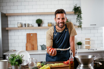 Happy smiling man preparing tasty meal. Young man cooking in the kitchen.