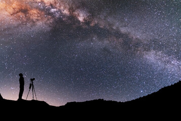 Wall Mural - the man silhouette with camera and tripod, stands on the hill and looking at the bright milky way ga
