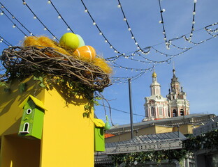 Wall Mural - Festive decoration of the city streets for the spring holidays - Nest with eggs and birdhouses.  happy Easter. Near the monastery
