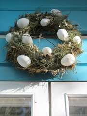 An Easter wreath decorated with Easter eggs hangs on the blue door.
