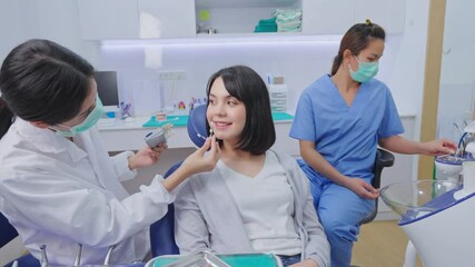 Wall Mural - Asian female dentist using tooth shade guide to compare tooth color.