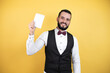 © Irene - Young man with beard wearing bow tie and vest smiling and showing blank notebook