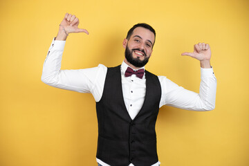 Wall Mural - Young man with beard wearing bow tie and vest looking confident with smile on face, pointing oneself with fingers proud and happy.