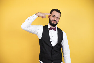 Wall Mural - Young man with beard wearing bow tie and vest Shooting and killing oneself pointing hand and fingers to head like gun, suicide gesture.