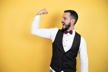 Wall Mural - Young man with beard wearing bow tie and vest showing arms muscles smiling proud