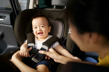Asian little baby happy and fun while fastened belt and seat in the safety car seat. A boy looking his mother and smile in a car.