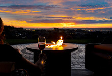 A Woman Drinks A Glass Of Wine In Front Of A Fire Pit On The Luxury Patio Of A Hillside Home Overlooking City Lights.