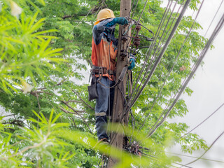 Brave man climb high working in the sun on dangerous job. Asian electrician wears hard hat helmet and safety tools standing on electric pole to maintenance power cable and electrical parts.