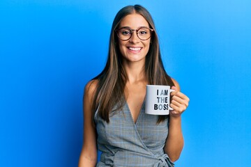 Young hispanic woman drinking from i am the boss coffee cup looking positive and happy standing and smiling with a confident smile showing teeth