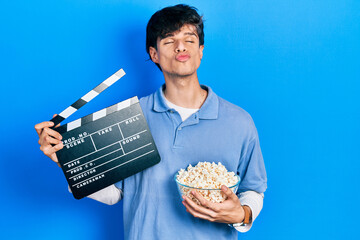 Sticker - Handsome hipster young man eating popcorn holding cinema clapboard looking at the camera blowing a kiss being lovely and sexy. love expression.