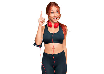 Sticker - Young redhead woman wearing gym clothes and using headphones pointing finger up with successful idea. exited and happy. number one.