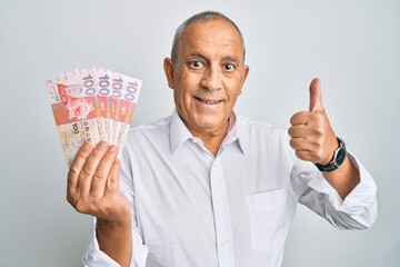 Poster - Handsome senior man holding 100 hong kong dollars banknotes smiling happy and positive, thumb up doing excellent and approval sign