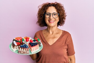 Poster - Beautiful middle age mature woman holding cake slices looking positive and happy standing and smiling with a confident smile showing teeth