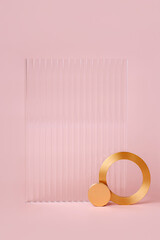 Wall Mural - Ribbed acrylic plate and  golden ring on pastel pink background. Stylish background for presentation.