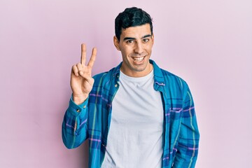 Handsome hispanic man wearing casual clothes showing and pointing up with fingers number two while smiling confident and happy.