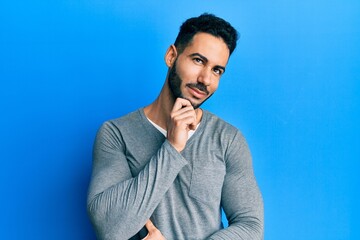 Young hispanic man wearing casual white t shirt thinking concentrated about doubt with finger on chin and looking up wondering