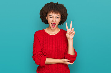 Young hispanic girl wearing casual clothes smiling with happy face winking at the camera doing victory sign. number two.