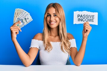 Sticker - Beautiful blonde young woman holding dollars and passive income text smiling with a happy and cool smile on face. showing teeth.