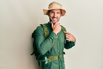 Canvas Print - Handsome man with beard wearing explorer hat and backpack looking confident at the camera smiling with crossed arms and hand raised on chin. thinking positive.