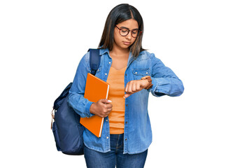 Young latin girl wearing student backpack and holding books checking the time on wrist watch, relaxed and confident