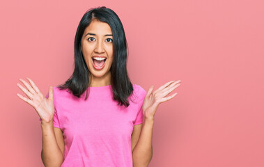 Beautiful asian young woman wearing casual pink t shirt celebrating crazy and amazed for success with arms raised and open eyes screaming excited. winner concept