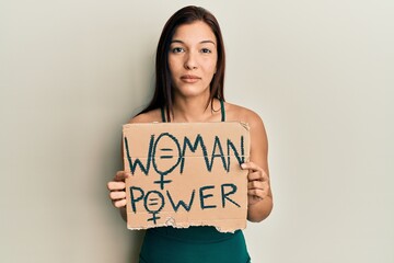 Poster - Young latin woman holding woman power banner relaxed with serious expression on face. simple and natural looking at the camera.