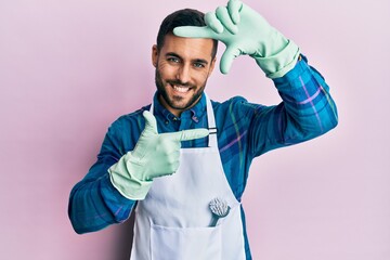 Poster - Young hispanic man wearing apron smiling making frame with hands and fingers with happy face. creativity and photography concept.