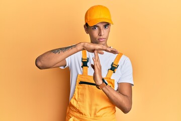 Poster - Young handsome african american man wearing handyman uniform over yellow background doing time out gesture with hands, frustrated and serious face