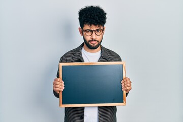 Canvas Print - Young arab man with beard holding blackboard skeptic and nervous, frowning upset because of problem. negative person.