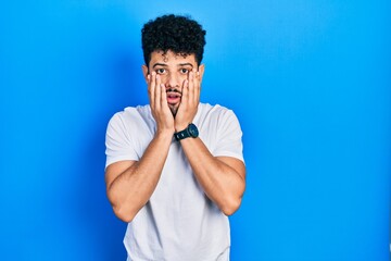 Canvas Print - Young arab man with beard wearing casual white t shirt afraid and shocked, surprise and amazed expression with hands on face