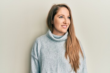 Young blonde woman wearing casual turtleneck sweater looking to side, relax profile pose with natural face and confident smile.