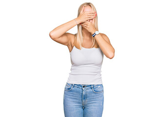 Sticker - Young blonde girl wearing casual style with sleeveless shirt covering eyes and mouth with hands, surprised and shocked. hiding emotion