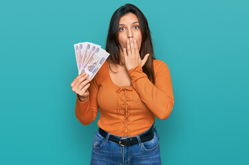 Poster - Beautiful hispanic woman holding russian 500 ruble banknotes covering mouth with hand, shocked and afraid for mistake. surprised expression