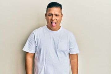 Young latin man wearing casual white t shirt sticking tongue out happy with funny expression. emotion concept.