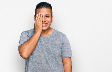 Young latin man wearing casual clothes covering one eye with hand, confident smile on face and surprise emotion.