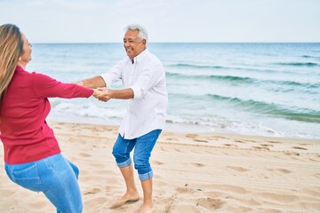 Middle age couple in love dancing at the beach happy and cheerful together