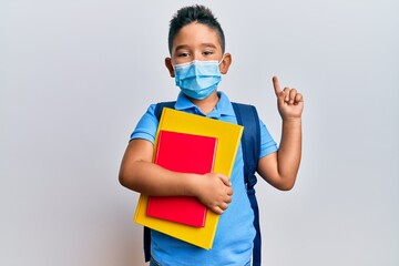 Sticker - Little boy hispanic kid wearing medical mask going to school smiling with an idea or question pointing finger with happy face, number one