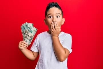 Sticker - Little boy hispanic kid holding 20 dollars banknotes covering mouth with hand, shocked and afraid for mistake. surprised expression